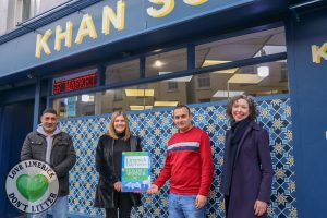 Two men and two women standing outside shop. One woman holding award sign